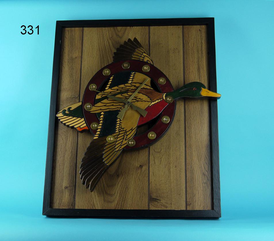 MALLARD CLOCK: WHIMSICAL CLOCK featuring a flying mallard encircled by 12 shot gun shell casings denoting the hours. The hands are brass shot guns. The whole mounted on a framed panel. Overall length of the mallard