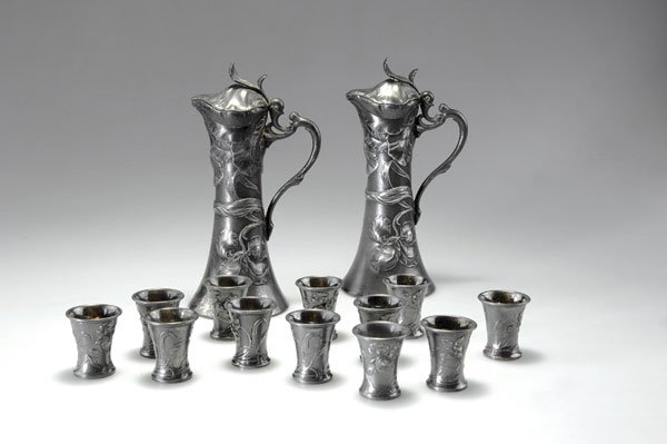 WMF, Geislingen: WMF, Geislingen. Pair of Liquor flasks with twelve glasses, c. 1900. Flasks, H. 22.7 cm; glasses, H. 4.8 cm. Britannia metal, silver-plated, insided gilded, reliefed pattern with iris. Marked: B, make
