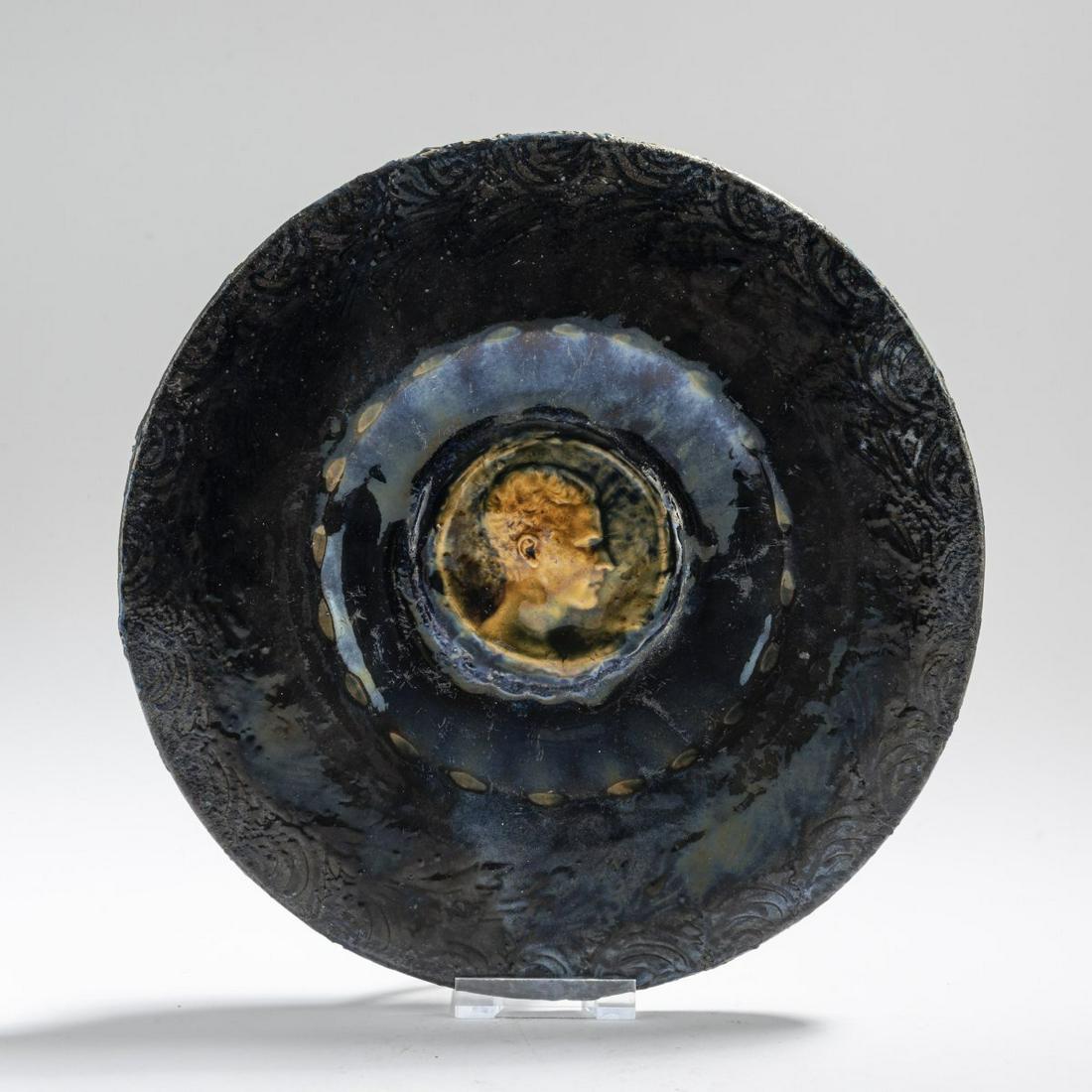 Hans Stoltenberg-Lerche, Decorative plate, 1910s: Hans Stoltenberg-Lerche, Decorative plate, 1910s, Ø 26.5 cm. Faience, dark blue and brown enamel. Medallion in relief in the middle. Roman style profile of a man. Edge with stylized leaves in b
