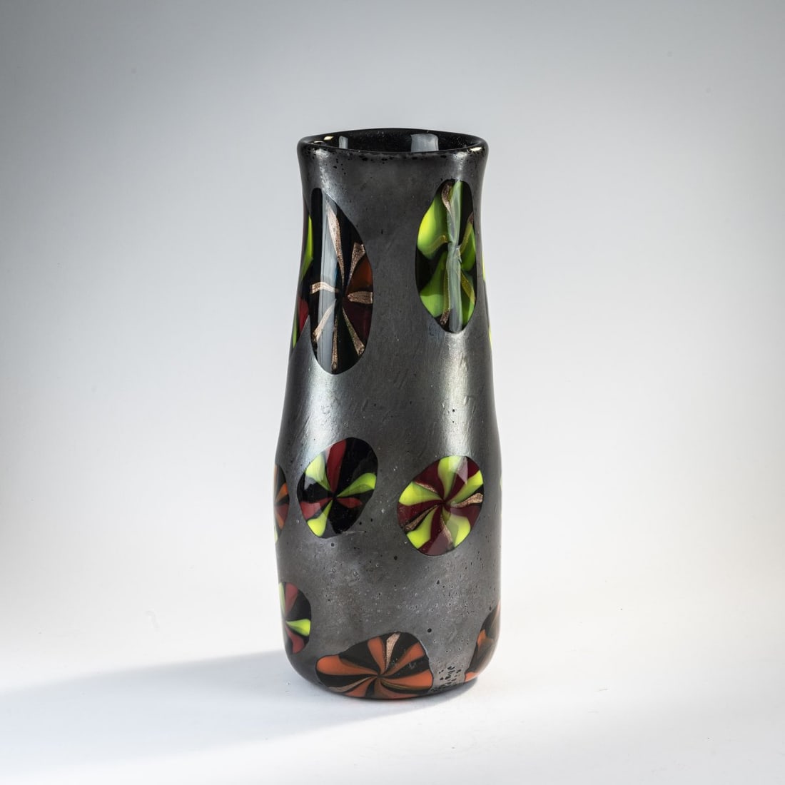 Pollio Perelda, 'Nerox stellato' vase, 1954: H. 41 cm. Execution: Fratelli Toso. Colorless glass, deep gray iridescent powder fusions, fused murrine in various colors. Literature: Cf. Marc Heiremans, Caterina Toso, Fratelli Toso, Stuttgart 2018