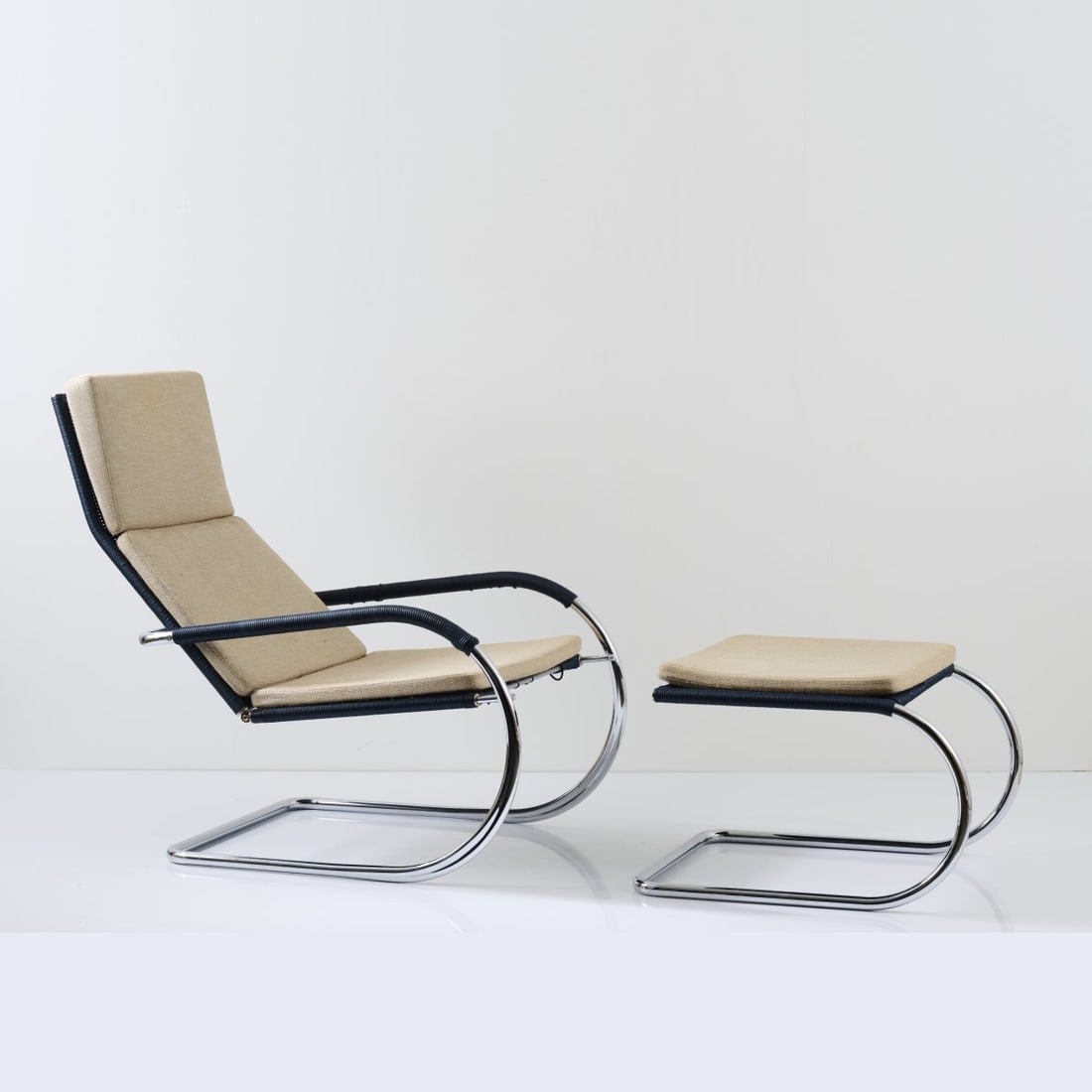 Anton Lorenz (after); Tecta, Lauenförde, 'D35-1i' armchair with 'C35i' ottoman, 1930s: Armchair: H. 96 x 65 x 88 cm; Ottoman: H. 43 x 68 x 54 cm. Made by Tecta, Lauenfoerde, 1990s. Tubular steel, chrome-plated, rattan weave, painted dark blue, beige fabric.