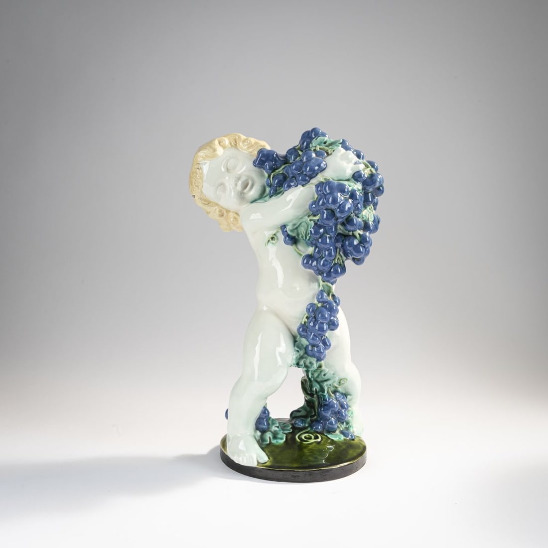Michael Powolny , 'Putto with grapes (autumn)', c. 1907: H. 37 cm. Execution: Wiener Keramik. Earthenware, glazed yellow, blue and green on white. Marked: Artist's signet, workshop signet (embossed). Literature: Neuwirth, Österreichische Keramik, Muni