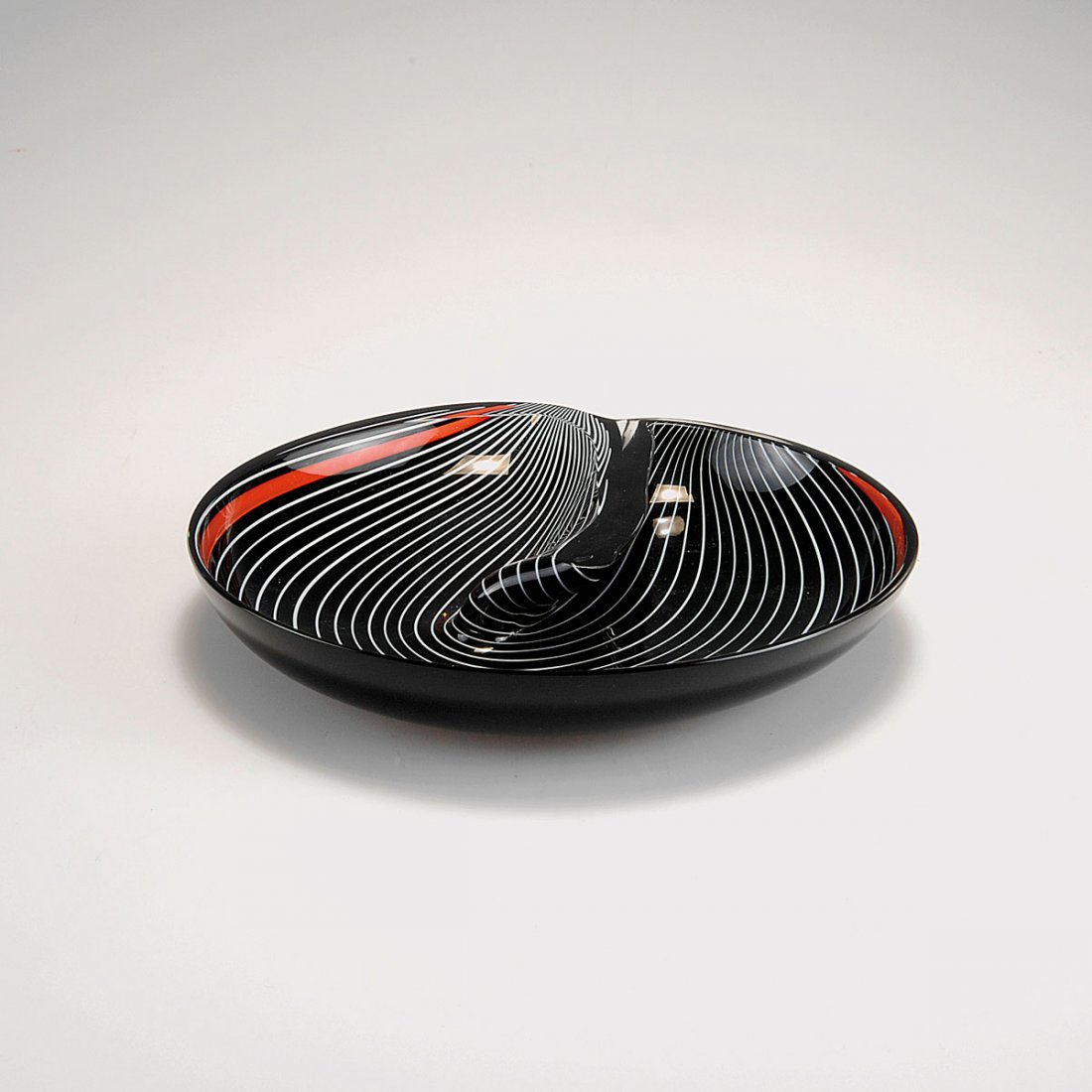 Bowl: Lino Tagliapietra. Bowl. Designed c1985. H. 3 cm; D. 18.8 cm. Made by Effetre Vetri di Murano Domenica Saija, Wehr (distributor). Cased glass, clear and black, included glass rods in white and red. Ma