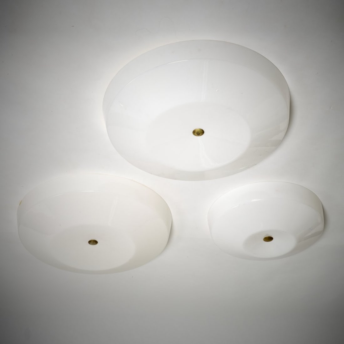 Yki Nummi, Three ceiling lights, 1960s: H. 14.5 cm, Ø 55-75 cm. Made by Sanka Oy, Loviisa. Sheet brass, white plastic. Marked: manufacturer's sticker.