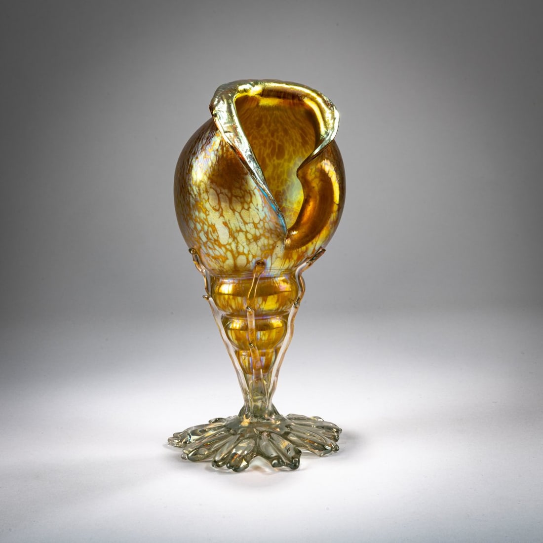 Loetz, Klastersky Mlyn, 'Papillon' shell vase, c. 1899: <p>H. 22 cm. Cased glass, colorless and amber, with rolled-in pieces of glass between the layers, matte gold and pearlescent luster, foot and applications made of colorless glass.</p>