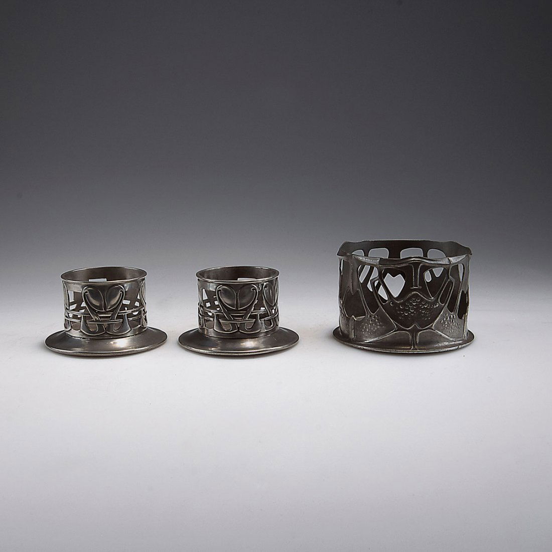 '0315' bottle coaster and pair of '0441' coasters, c190: William Haseler, Birmingham. '0315' bottle coaster and pair of '0441' coasters, c1902-05. H. 5.2-5.8 cm. Made for Liberty & Co., London. Pewter. Marked: TUDRIC, 0315 resp. 0441, coaster add.: Rd. 4275