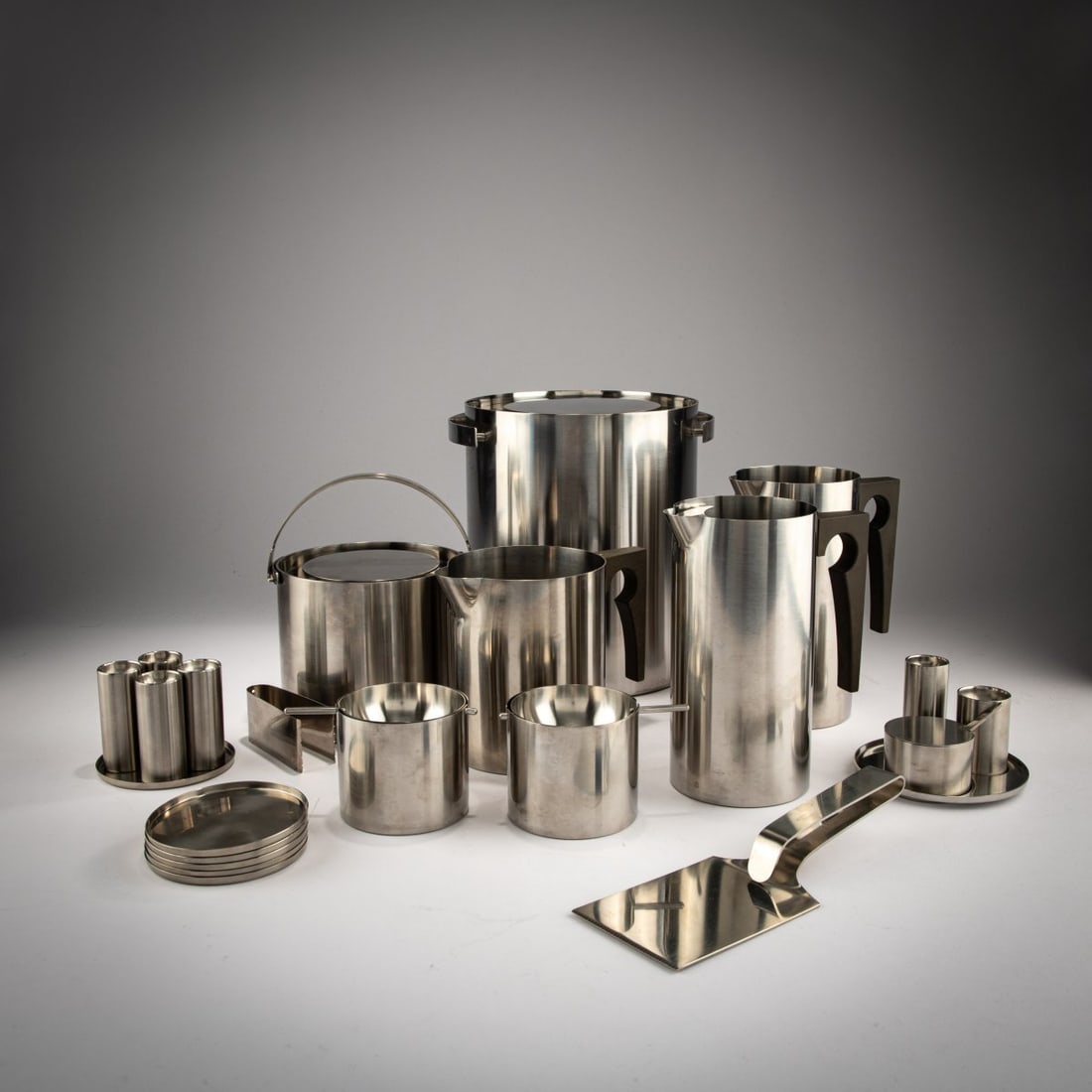 Arne Jacobsen, 24 kitchen pieces from the 'Cylinda Line', 1967 (design): <p>3 jugs, 2 ice buckets, ice tongs, ice lifter, 4 pepper and salt shakers, spice set consisting of pepper and salt shakers and a mustard pot with spoon on a tray, 6 nut bowls in the original