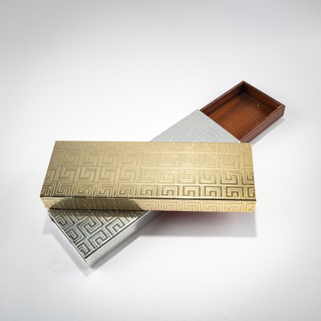 Piero Fornasetti, Two cigarette boxes 'Greca incisa', 1950s-60s: <p>Each 3 x 29.5 x 10 cm. <br />Fornasetti, Milan. <br />Pressed metal sheet with meander decoration, silver and gold colored, mahogany. <br />Marked: Brush mark