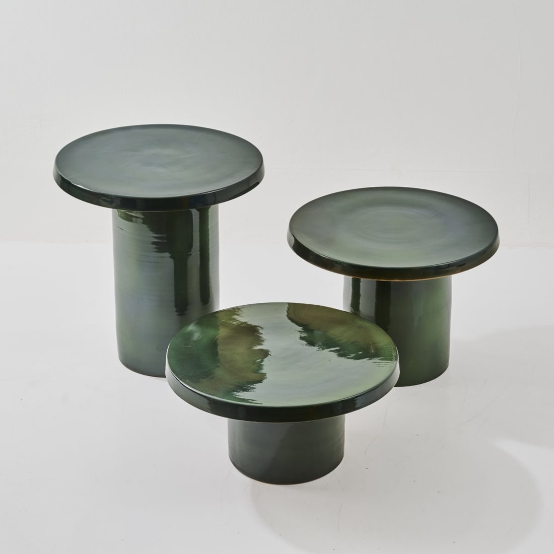 Italy, Three occasional tables, 1970s: <p>H. 29 - 52 cm, &Oslash; 50 cm. <br />Earthenware, glazed dark green.</p>