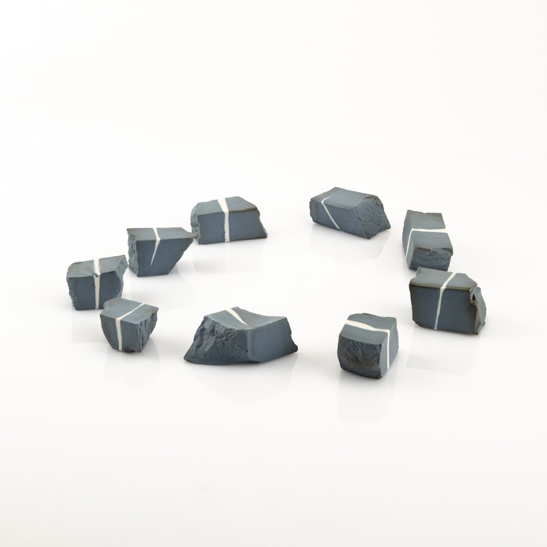 Piet Stockmans (1940 Leopoldsburg - lives and works in Genk), 9 Untitled Porcelain Objects, 1988: <p>Nine hard-paste porcelain objects, fired using the reduction firing method, in a wooden box. H. 4.0 x 4.3 x 3.0 cm to 8.0 x 3.5 x 3.0 cm (stones), 5.0 x 45.0 x 5.6 cm (box). Signed on one sto