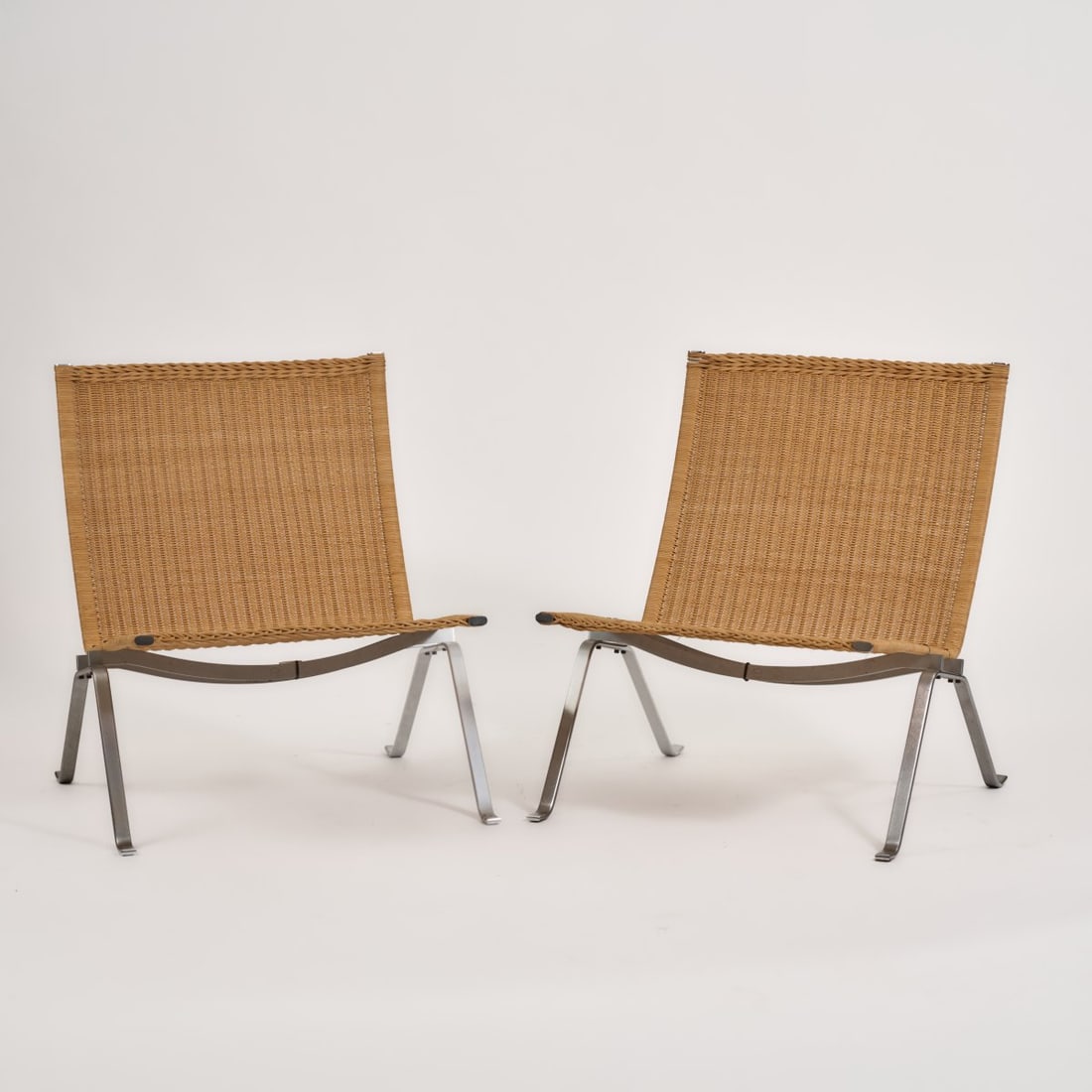 Poul Kjaerholm, Two armchairs 'PK 22', 1955 (design): <p>H. 72.5 x 64 x 63 cm. <br />Fritz Hansen, Aller&oslash;d, 1992.<br />Steel strip, matt chrome-plated, rattan weave. <br />Marked: Manufacturer's and serial number