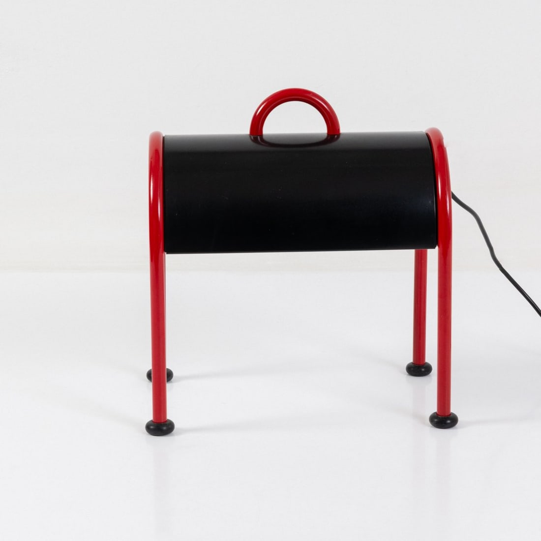 Ettore Sottsass, Table light 'Valigia', 1977 (design): <p>H. 37,5 x 35 x 23,5 cm.<br />Stilnovo, Milan.<br />Tubular metal, lacquered red, sheet metal, lacquered black, black rubber. <br />Marked: Manufacturer's label.</p><