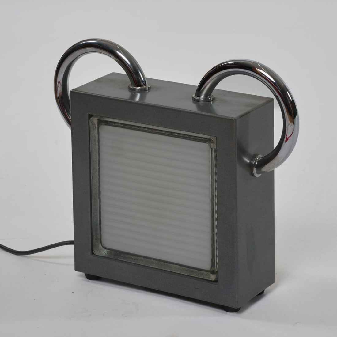 Matteo Thun, Table light 'Topolino' from the 'Loftlight' series, 1989 (design): <p>H. 34 x 39 x 10.5 cm. <br />Bieffeplast, Padua. <br />Chrome-plated steel tubing, gray lacquered sheet steel, colorless and white safety glass. <br />Marked: Manufacturer's 