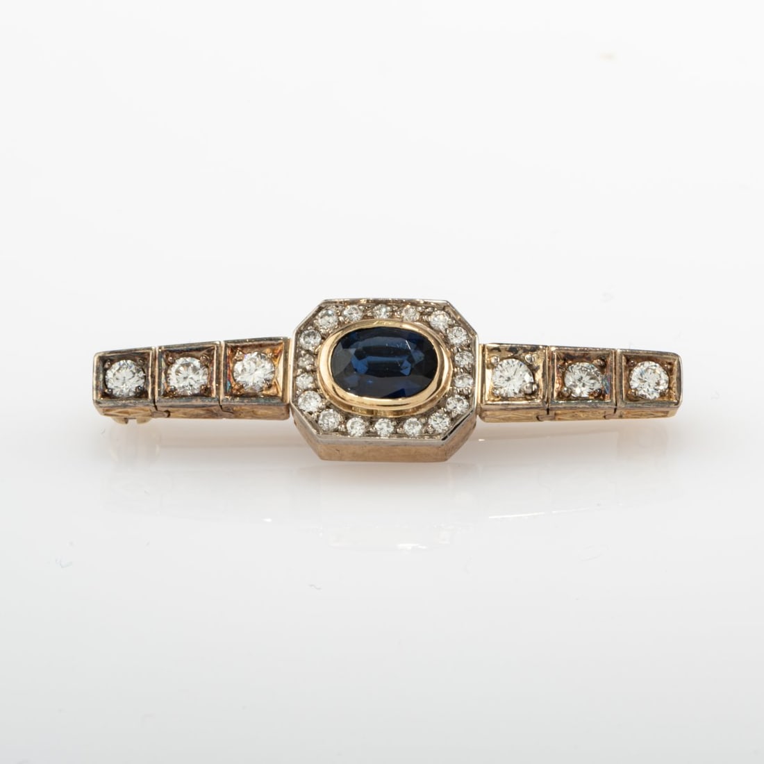 , Brooch with sapphire and diamonds: <p>Yellow and white gold, oval-cut sapphire (approx. 0.62 ct., calculated weight), 24 diamonds (total approx. 0.45 ct., calculated weight). <br />5.54 grams. 37 x 10 mm. </p>