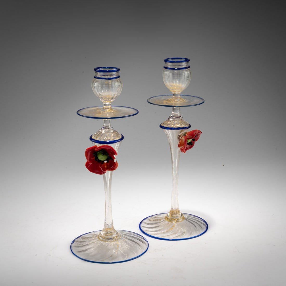 Vetreria artistica Barovier & C., Murano, Pair of candlesticks, 1910: <p>H. 25.6 cm. Colorless glass with burst gold foil, blue bands applied to the rims, applied poppies made of red, green and dark purple glass. </p>
