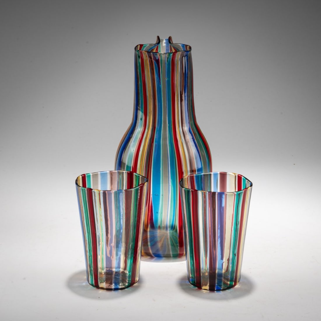 Gio Ponti, Carafe with two glasses 'A canne', 1946/47: <p>Model No. 915/0 and 915c. H. 11 cm and 24 cm. Execution: Venini. Colorless glass with fused vertical bands in blue, red, green, violet, and yellow. </p>
