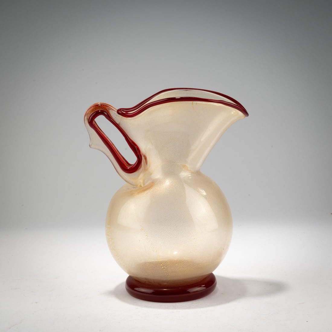 Ercole Barovier, 'Eugeneo' jug, 1951: <p>H. 18 cm. Execution: Barovier &amp; Toso, Murano. Glass, colorless, with finely burst gold foil; base, rim, and handle loops red.</p>