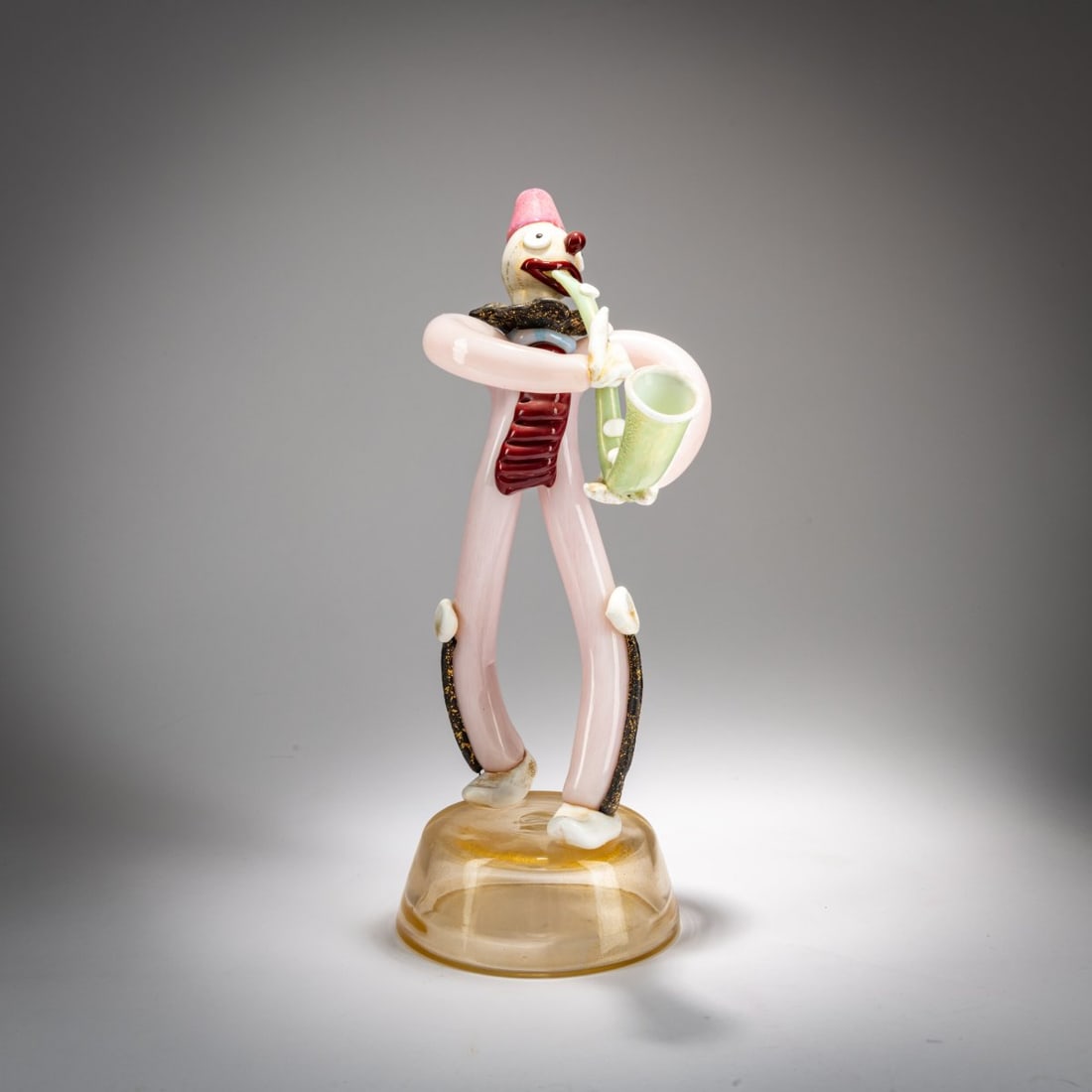 Fratelli Toso, Saxophone player, 1956: <p>H. 32 cm. Colorless glass with pink and green powder inclusions; white, black, and red glass paste. Colorless base, partially covered with gold foil.