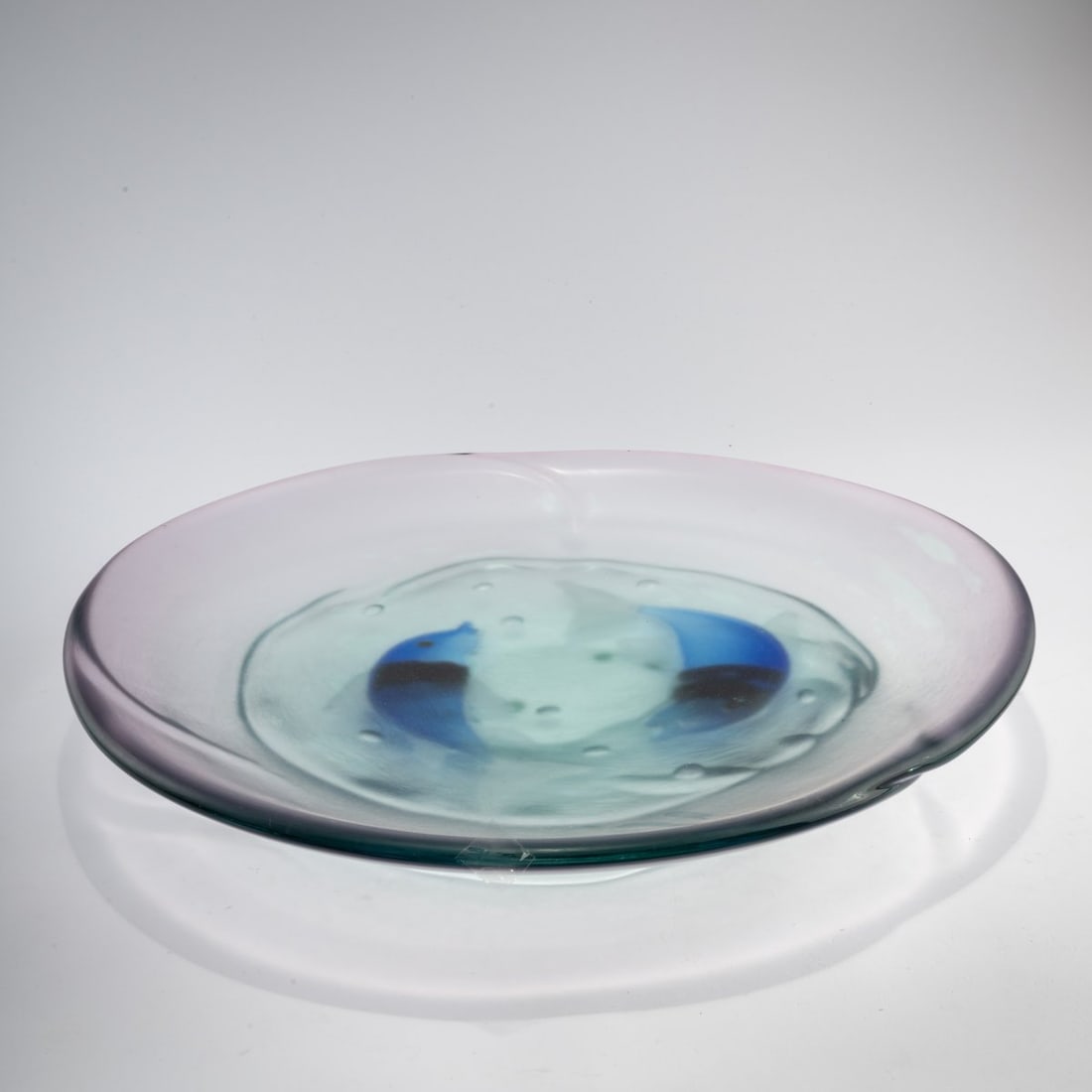Alfredo Barbini, Decorative plate 'Pesci', c. 1960: <p>51 x 52.5 cm. Thick-walled cased glass, colorless, slightly pinkish-red. Fish in dark blue, yellow, and violet with opalescent white rods are fused into the center. Bottom marked: A. Barbini