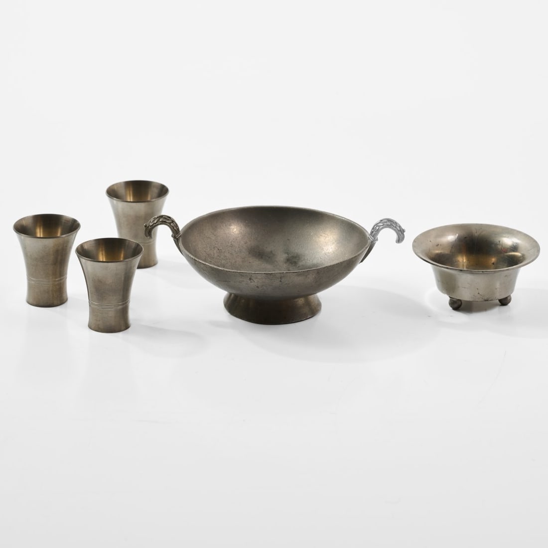 Paavo Tynell, Three shot glasses and two bowls, 1930s/1940s (design): <p>Glasses: H. 4.5 cm, &Oslash; 4 cm; bowls: H. 3 &ndash; 4 cm, &Oslash; 8 &ndash; 16 cm. <br />Taito Oy, Vilhonvuorenkatu.<br />Pewter.<br />Marked: