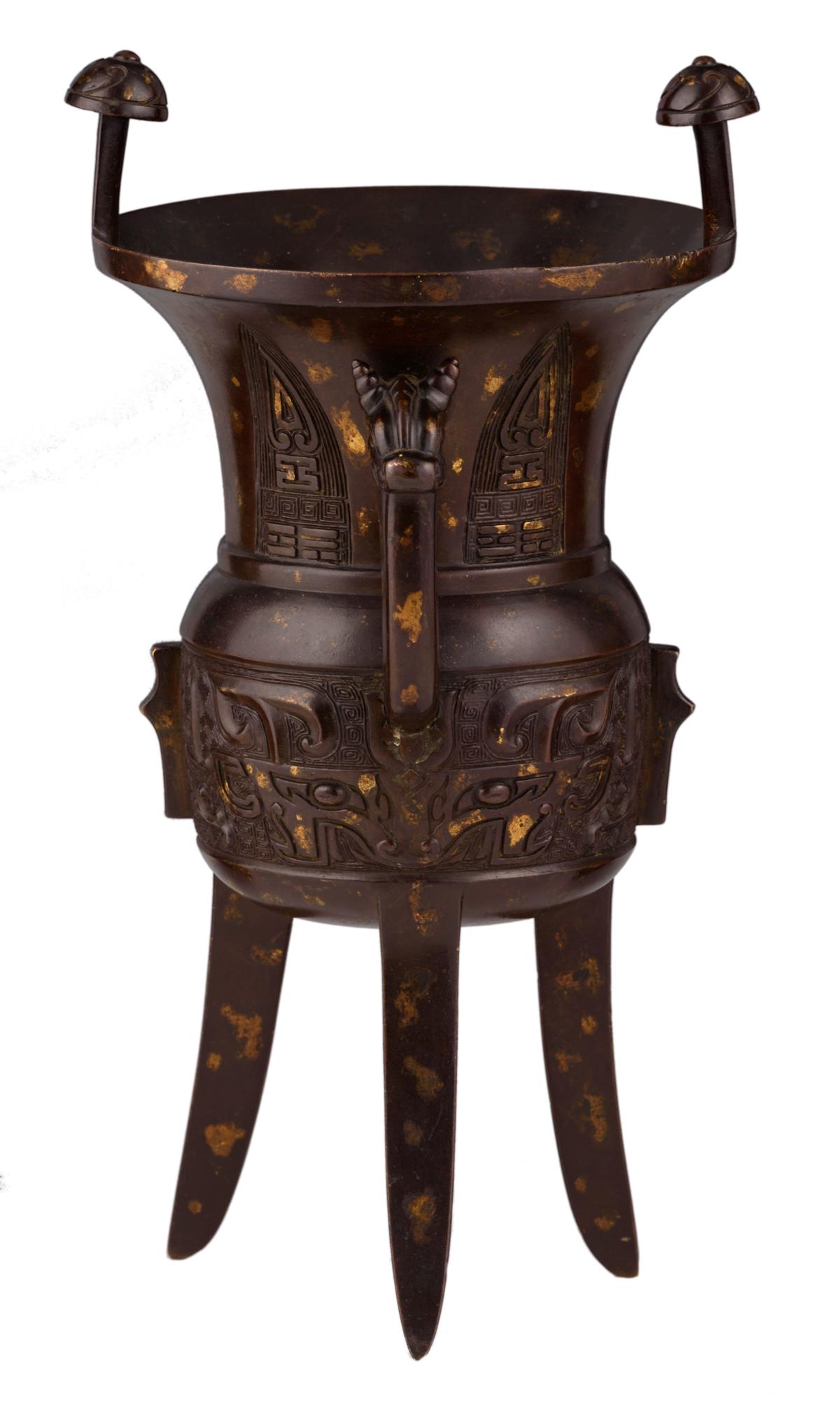 An archaic bronze gold-splash decorated Jia tripod: An archaic bronze gold-splash decorated Jia tripod vessel, relief decorated with Taotie masks and the Eight Trigrams, marked, probably 17th/18thC, H 31 cm