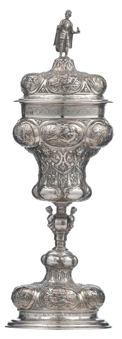 An imposing English Renaissance Revival silver cup with: An imposing English Renaissance Revival silver cup with assorted cover, the domed foot as well as the body decorated with embossed and engraved lobes, alternately depicting hunting scenes and mytholog