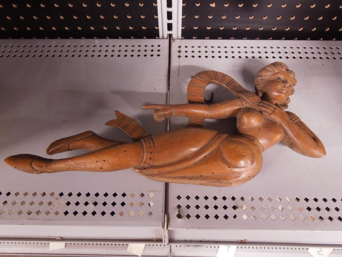 Carved Wood Woman Figure: Carved wood woman figure, reclining woman with crossed legs holding ribbon, glass eyes, 19th C 17" x 8" h CONDITION: normal wood wear, old worn holes throughout, hairline crack on neck
