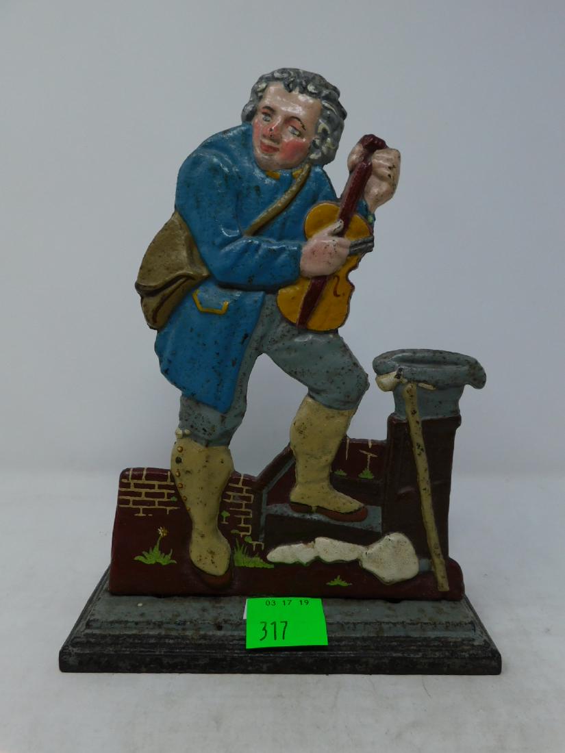 Cast Iron Doorstop Man with Violin: Cast Iron Doorstop Man with Violin: A cast iron doorstop of a man in 18th century costume with a sachel and a fiddle or violin. He stands with one foot on brick stoop against which his walking stick l