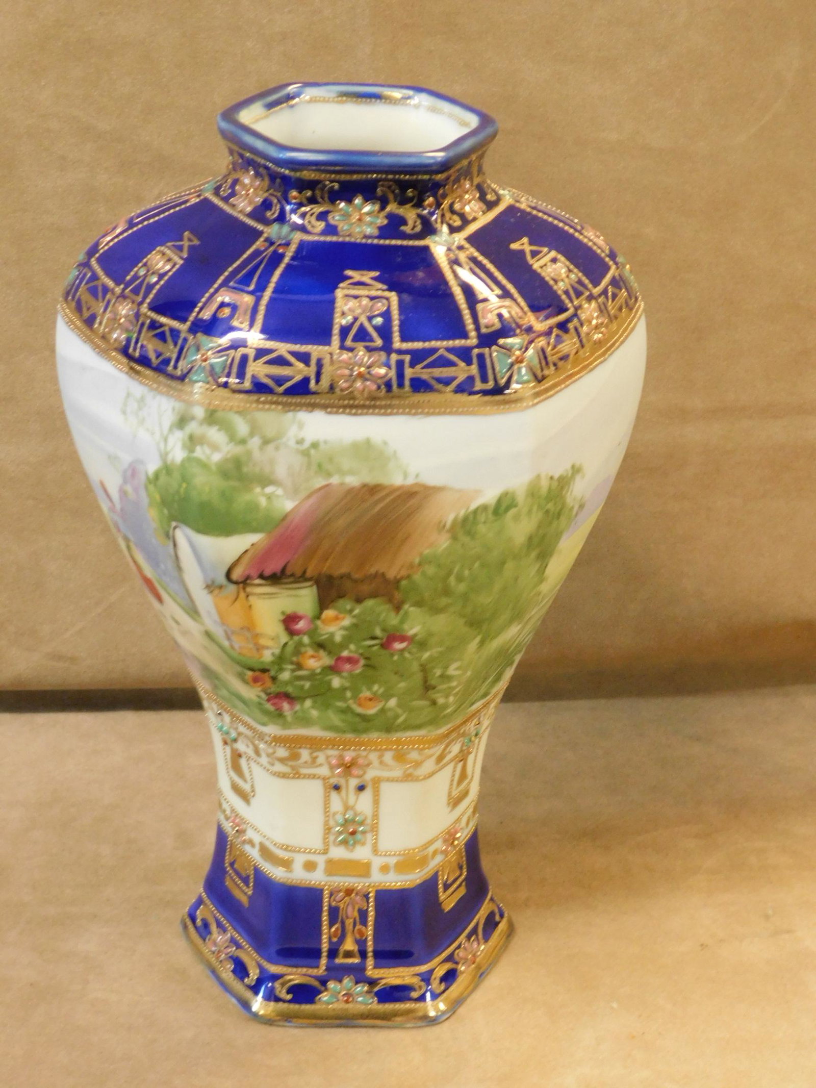 Nippon Porcelain Hand-Painted Vase: Nippon Porcelain Hand-Painted Vase. A fine large Japanese porcelain vase of hexagonal baluster form, hand-painted with a large scene of a female peasant and a cottage in a large scenic landscape, surr