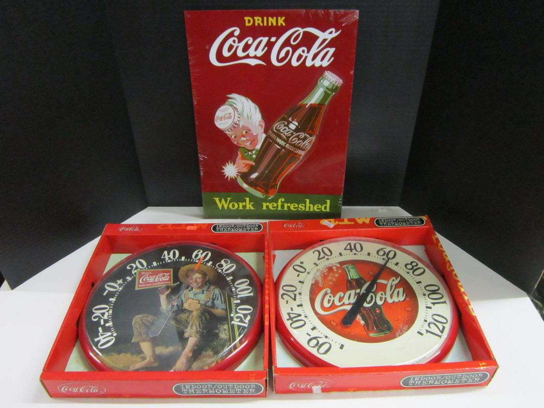 2 Coca Cola Thermometers & Tin Sign: Two Coca Cola Thermometers & Tin Sign, all in original packages of factory sealed including: two indoor - outdoor thermometers (one with Coca Cola bottle and one with Country Box, 12 1/2"d, plus "Drin
