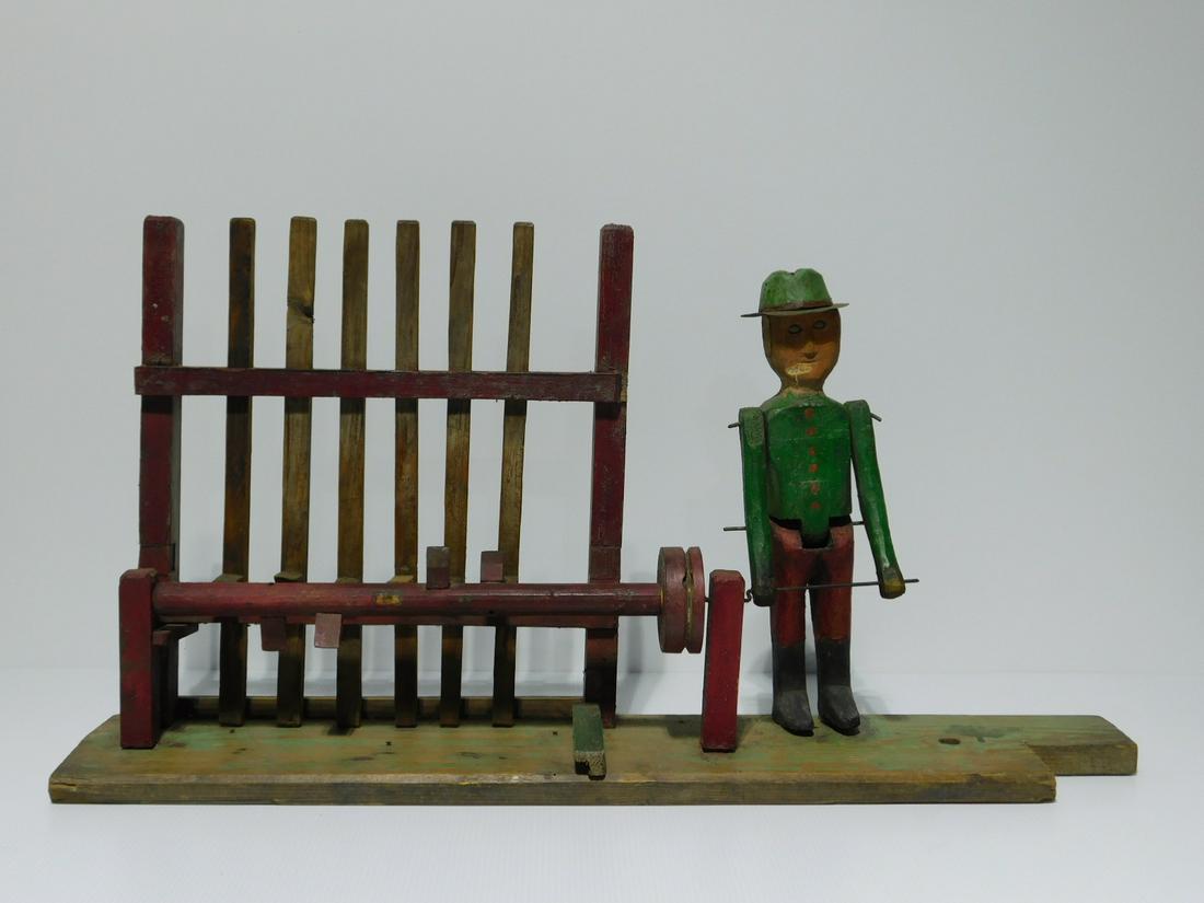 Folk Art Wooden Whirligig: Folk Art Wooden Whirligig, in the form of a many working a crank turning a shaft with a series of cams which activate six vertical posts or trip-hammers. Shaft has a pulley on it with a groove for a b