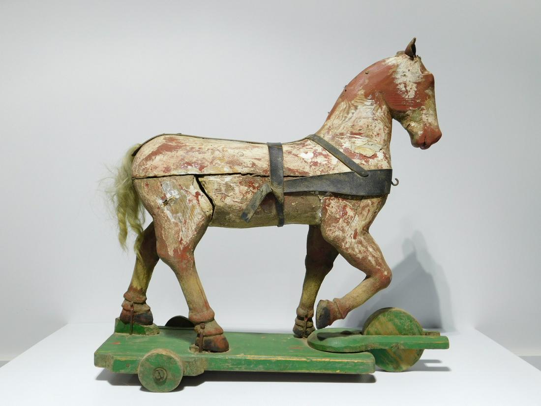 Antique Ride-On Folk Art Horse Toy: Antique Ride-On Folk Art Horse Toy, hand-carved, possibily a figure from a small-scale carousel, mounted on a later wooden three-wheeled base. The horse with leather ears and applied trappings, remain