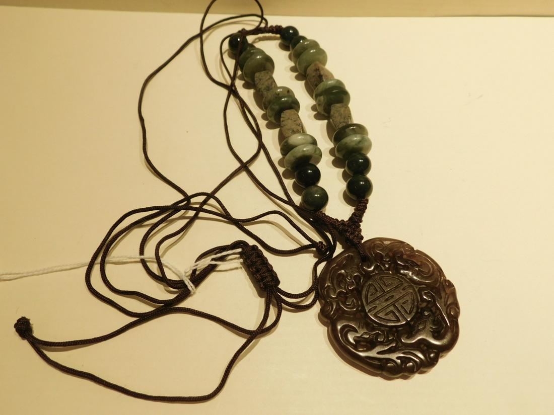 Chinese Jade and Hardstone Necklace: Chinese jade and hardstone necklace, Carnelian color jade pierce carved 2 1/4" diameter Dragon pendant with attached knotted brown string embellished with varying shaped green hearthstones beads, earl