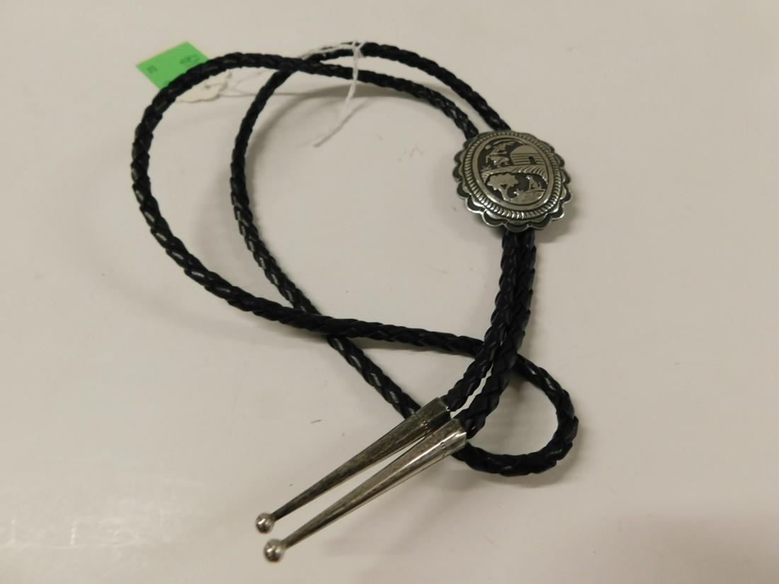 Navajo Bolo Tie: Navajo Bolo Tie, silver with relief dancing Indian and howling wolf, oval, 1 1/2" x 1 7/8", leather cord and silver tips. Condition; very good