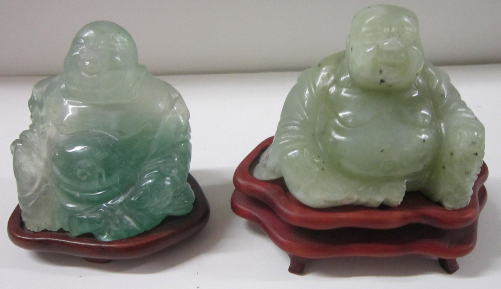 Two Green Hardstone Seated Laughing Buddhas: Two Green Hardstone Seated Laughing Buddhas, both hand-carved, one likely jadeite, both on fitted wooden stands. Chinese, 19th / 20th C. largest is 4 3/4" wide by 4 1/4" tall overall. CONDITION: Both 