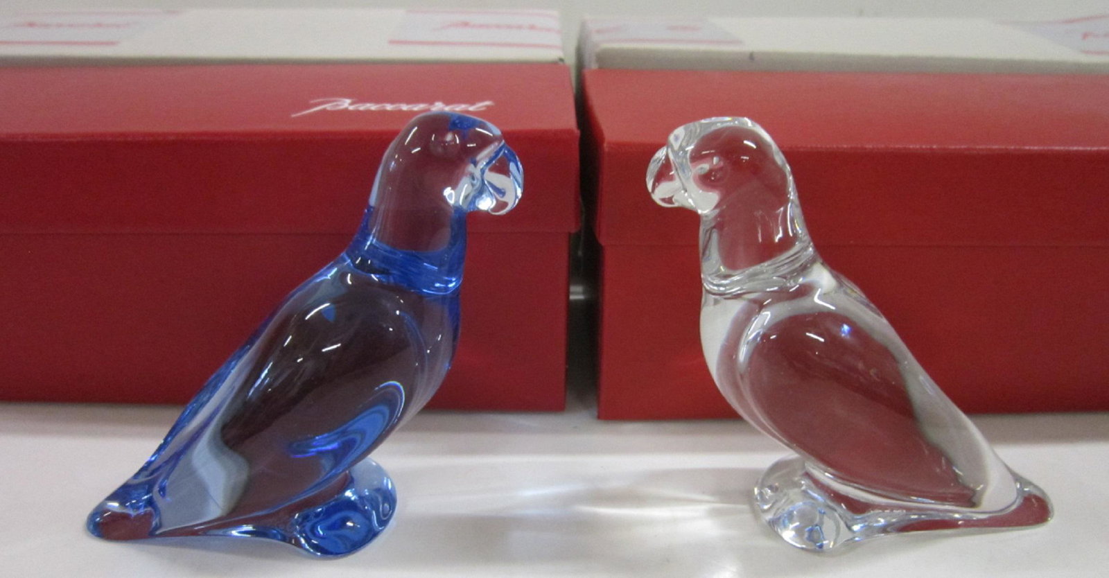 2 Baccarat Parrots Figures: Two Baccarat Parrots Figures, France, includes: corn flower blue crystal parrot and a clear crystal parrot; 4" h, both in their original boxes. CONDITION: Like new condition.