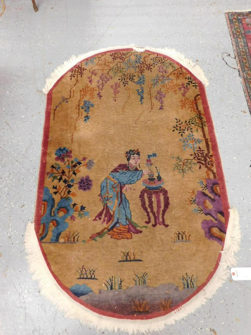 Chinese Throw Rug: Chinese throw rug oval, gold field with Geisha at plant stand in a floral surround, early 20th c. 36" x 56". CONDITION: Refringed ends, slight areas of wear and spots where white threads show through.