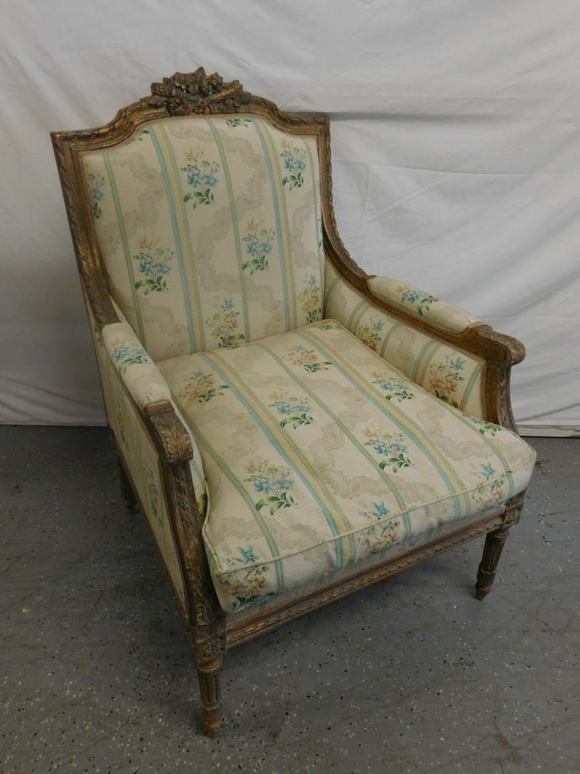 Louis XVI Style Bergere Chair: Louis XVI Style Bergere Chair, distressed gilt finish, serpentine crest with floral and torch carvings, floral and stripped cloth upholstery, acanthus carved arm supports, reeded and turned legs with 