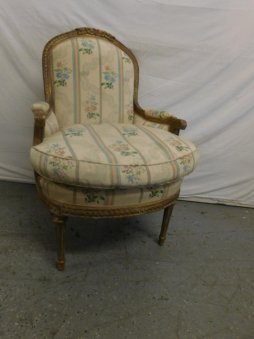 Louis XVI Style Bergere Chair: Louis XVI Style Bergere Chair, distressed gilt finish, rose carved crest on an arched back, wide demi lune seat, stripped and floral cloth upholstery, reeded and turned legs, early 20th C, 40"h. CONDI