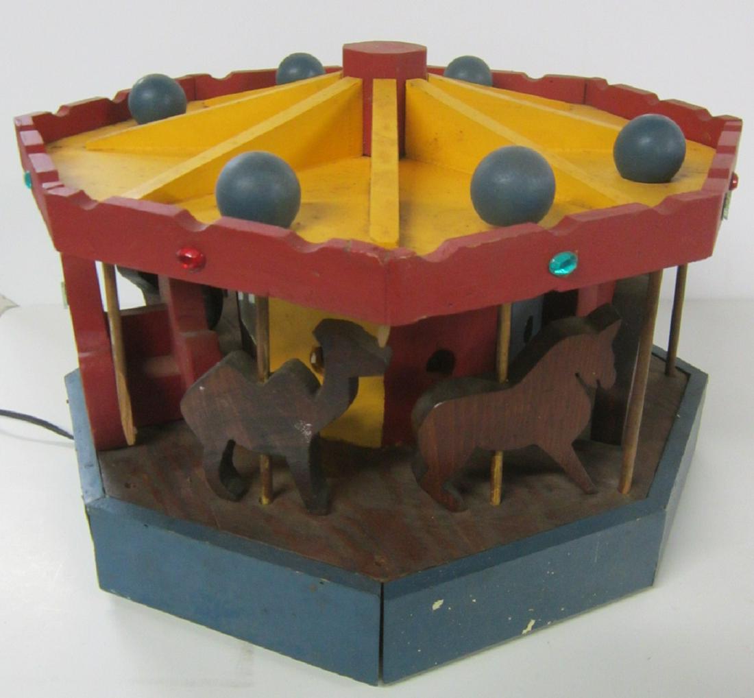 Lighted Wood Revolving Carousel: Lighted Wood Revolving Carousel, red, yellow and blue painted with cut out carousel animals and seats, jeweled top, plug in cord for inside light, 16"d x 12"h. CONDITION: Lights, rotates freely, two s