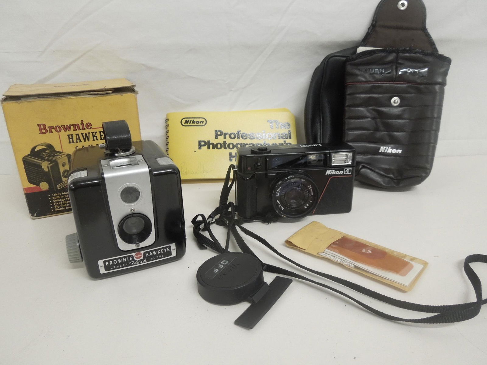 2 Cameras: Two Cameras includes: Brownie Hawkeye flash model camera in original box (no flash attachment); and a Nikon L35 AF camera with case and Nikon L35AF camera with case and "Nilon The Professional Photogr