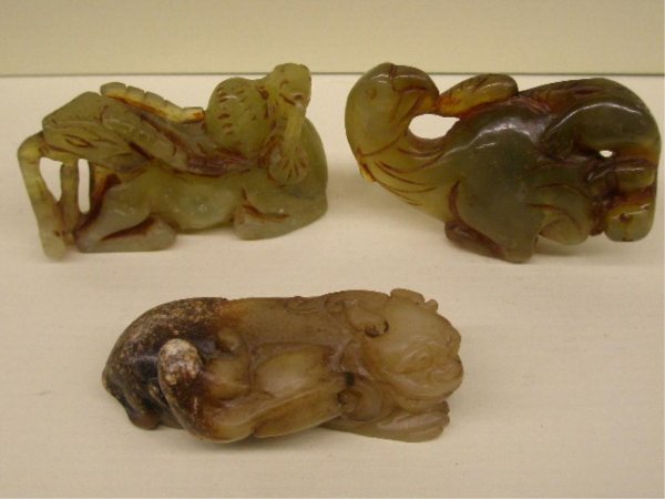 Three Chinese Jade Animal Carvings: Three Chinese jade animal carvings, 1) Celadon green jade seated ram with animal on his back, 3" x 1 3/4", 2) Multi colored green jade bird with unknown animal, 3 1/8" x 2", 3) Cram to brown jade Foo 