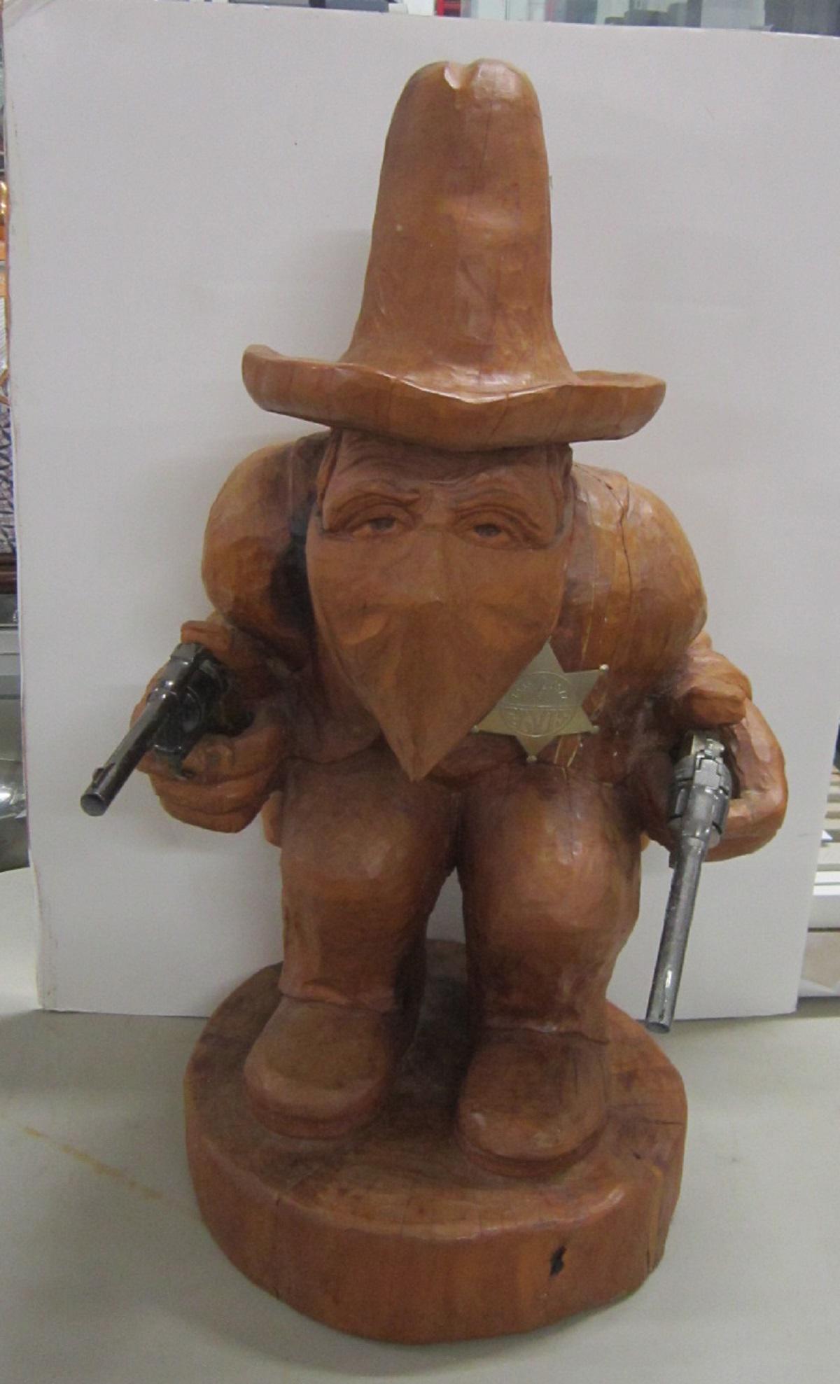 Mexican Carved Wood Cowboy: Mexican carved wood cowboy, large scale one piece carving of squatted gun slinging cowboy with Sombrero; he holds two "Super Cowboy" metal cap guns and wears an Elvis 1977 Star Badge, 20th c, 28"h, ap