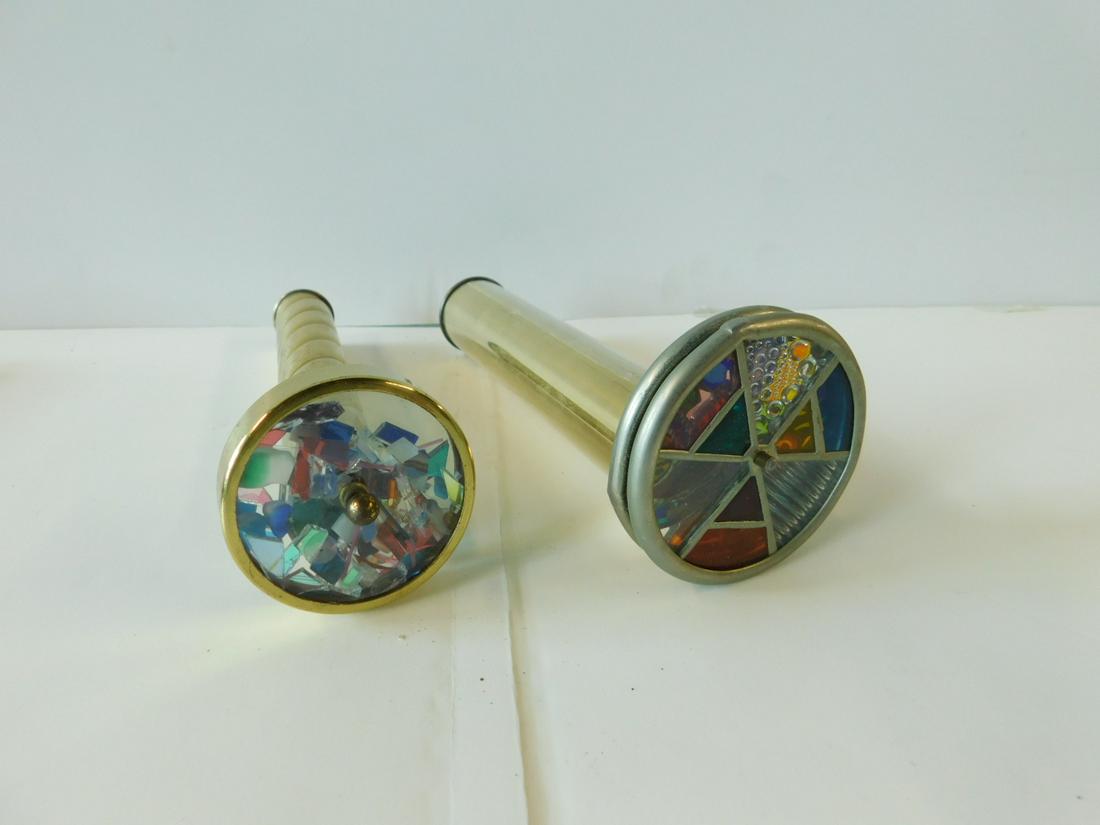 2 Brass Tubular Kaleidoscopes w/Wheels: Two Brass Tubular Kaleidoscopes w/Wheels, one 9" swirl design on tube w/single wheel w/glass shards. One 9" w/double leaded stained glass wheels. [9] CONDITION: Fair with some pitting and scratches.
