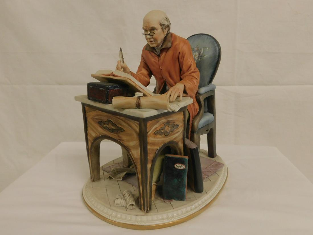 Capo di Monte Figurine: Capo di Monte Figurine, artist signed Volta, seated elderly spectacled scribe with pen and book at table, 20th C, 9" x 9 1/2" x 6 1/2". CONDITION: No issues identified.