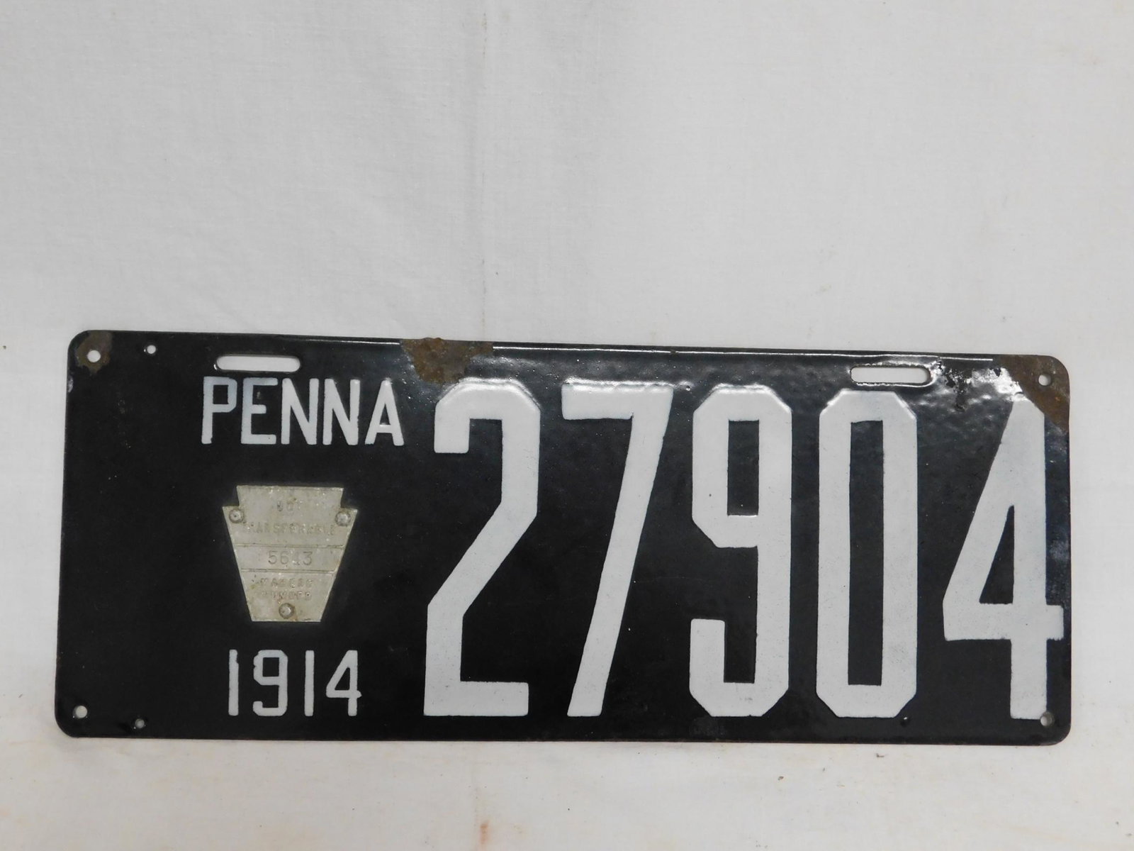 1914 Pa. Porcelain License Plate: 1914 Pa. Porcelain License Plate, black with white letters and numbers, 27904 with attached metal Keystone makers plaque #5643, Brilliant Mfg. Co., Phila, PA, 6" x 15". CONDITION: Spots of enamel loss