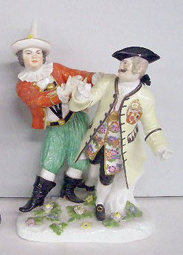 19th c. Meissen Porcelain Figure Group: Early 19th c. Meissen hand painted porcelain 9 1/2" x 7 1/2" figure group depicting comedic & elegant dressed conjoined men standing on a tree stump base w/applied flowers, comedic dressed man is hold