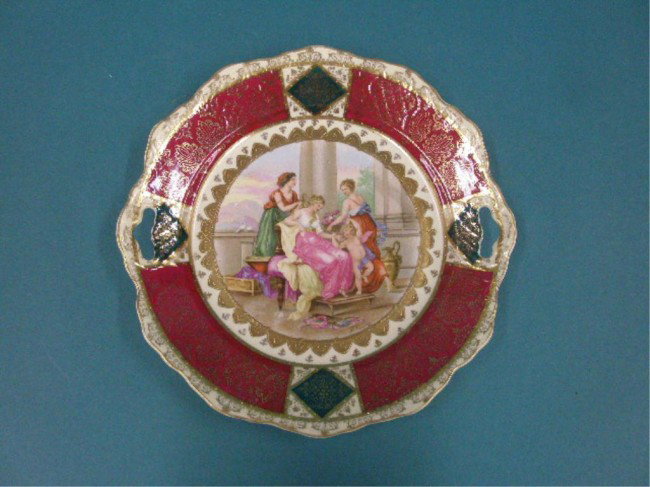 Austrian Porcelain Cake Plate: Austrian porcelain 10" double handle cake plate w/transfer & hand painted allegorical figural scene in center, painted gilt fleur de lis on maroon panel border, artist signed A. Kauffman