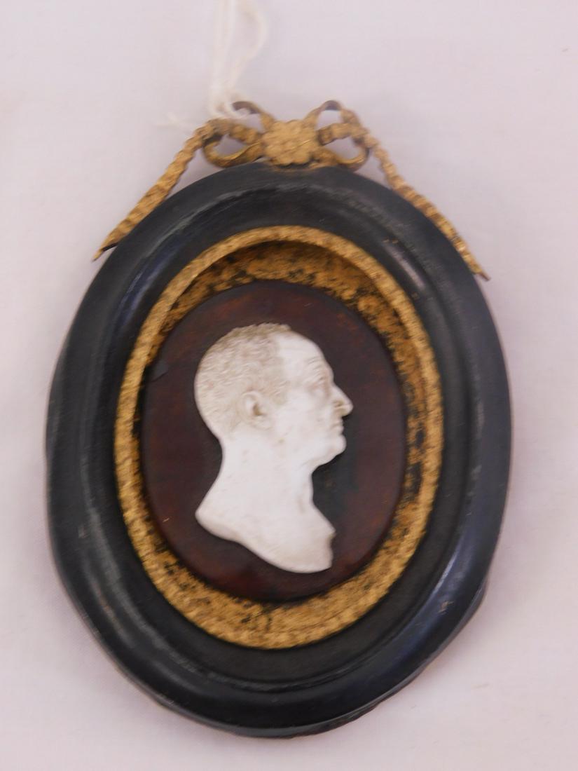 19th C. Miniature Portrait Plaque: 19th C. Miniature Portrait Plaque, a milk glass silhouette portrait of a Roman ? nobleman mounted on an amber glass oval panel and set into a non conforming gilt metal and black lacquered oval frame, 