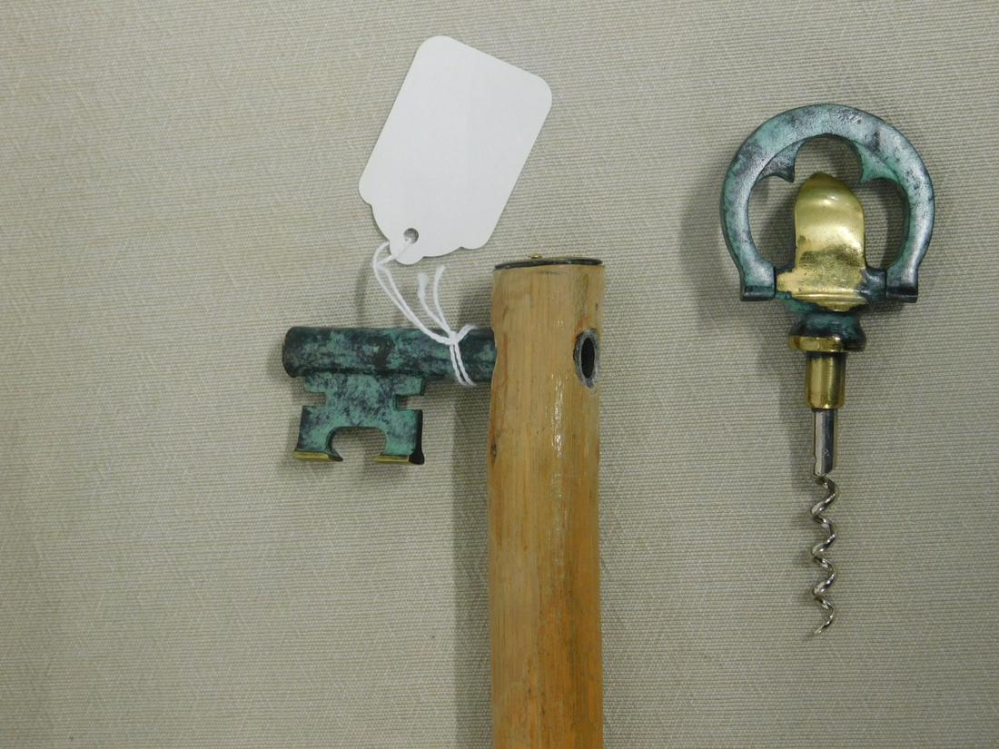 Key / Corkscrew Handle Cane: Key / Corkscrew Handle Cane. Handle: "T" shape brass with green patina in form of a key that pulls apart to a corkscrew and bottle opener. Shaft: knotty pine crested with brass escutcheon. Ferrule: Co